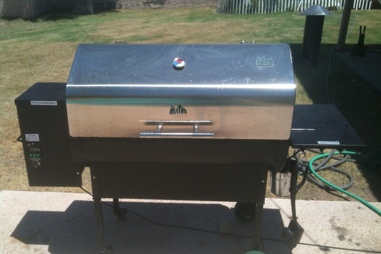 A pellet grill with side shelf on an outdoor patio.